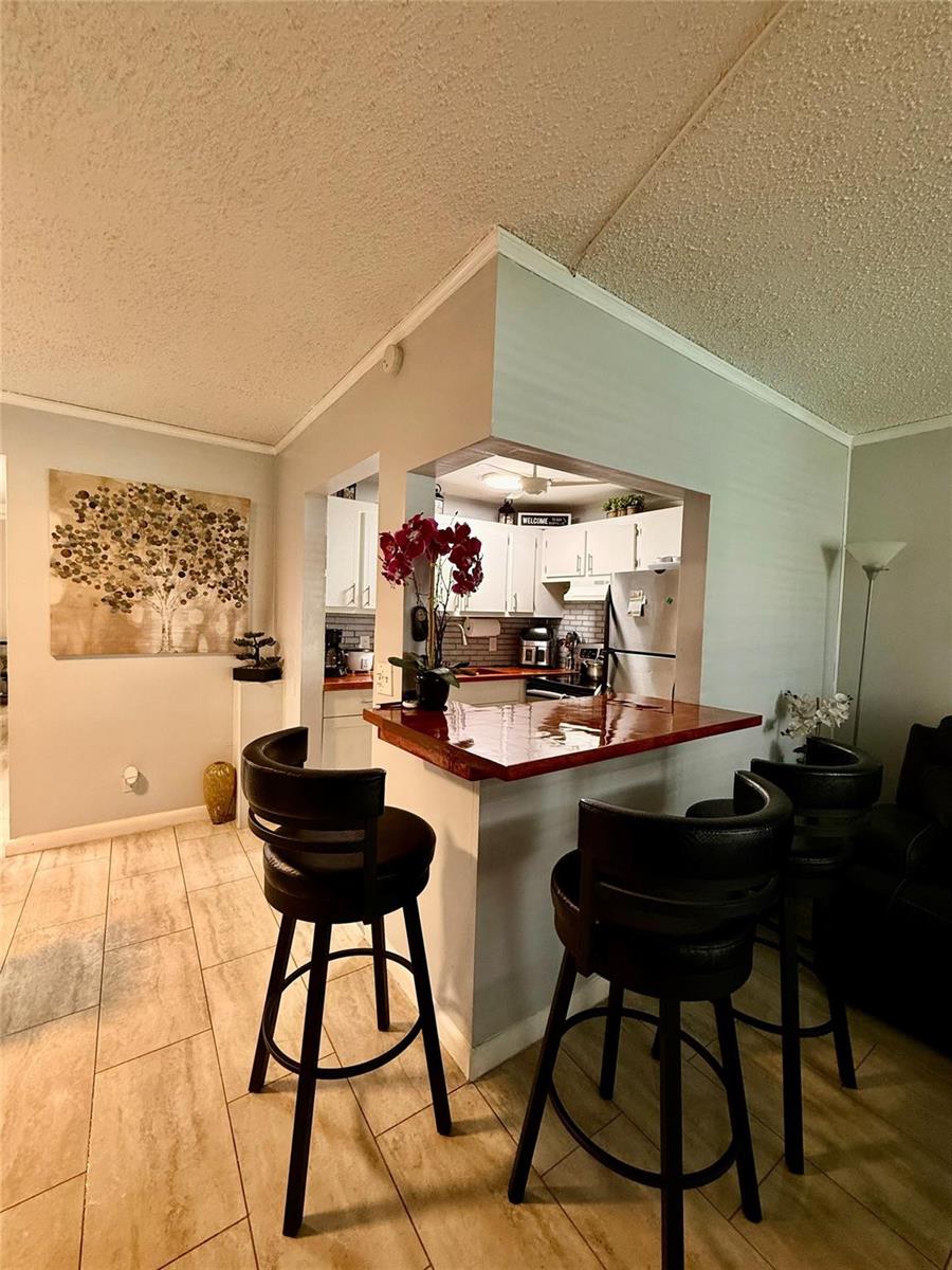 A kitchen with white cabinets and a wooden breakfast bar overlooks a living area — 355 Oakridge T # 355, Deerfield Beach FL 33442, DEERFIELD BEACH, FL
