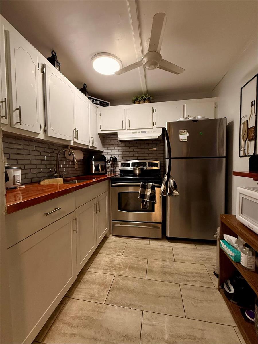 A kitchen features white cabinets, a wood countertop, stainless steel appliances, and gray tile backsplash — 355 Oakridge T # 355, Deerfield Beach FL 33442, DEERFIELD BEACH, FL