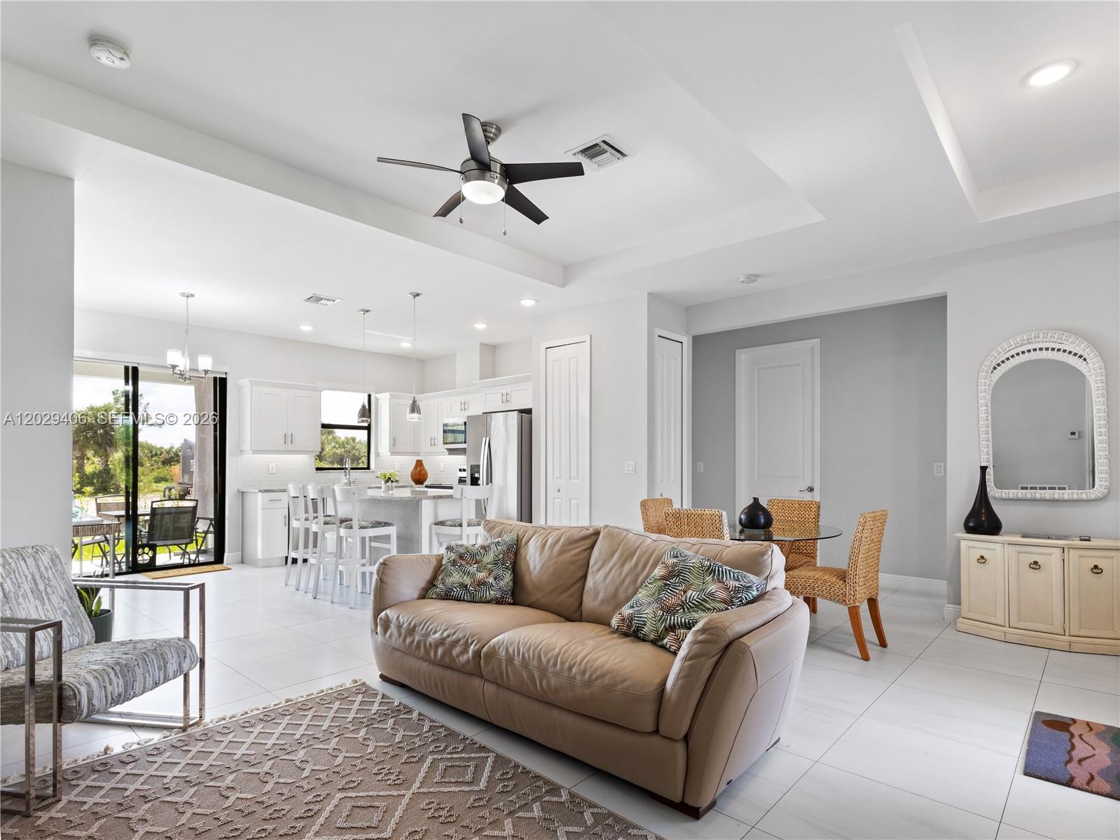An open-concept living and dining area features white cabinetry, tile flooring, and a leather sofa — 490 NW 37 AV., Naples FL 34120, NAPLES, FL