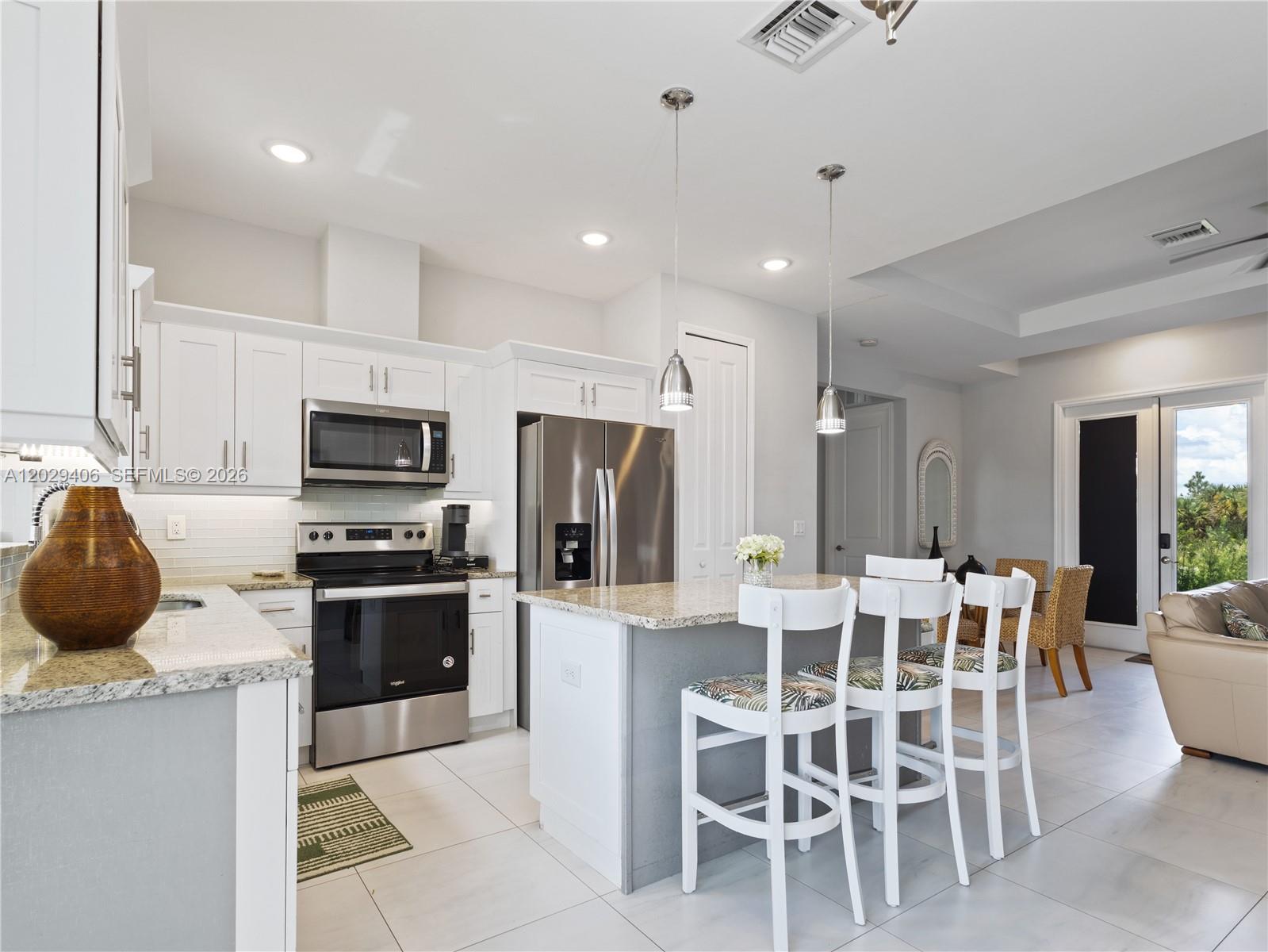 A modern kitchen features white cabinets, stainless steel appliances, a granite island, and bar seating — 490 NW 37 AV., Naples FL 34120, NAPLES, FL