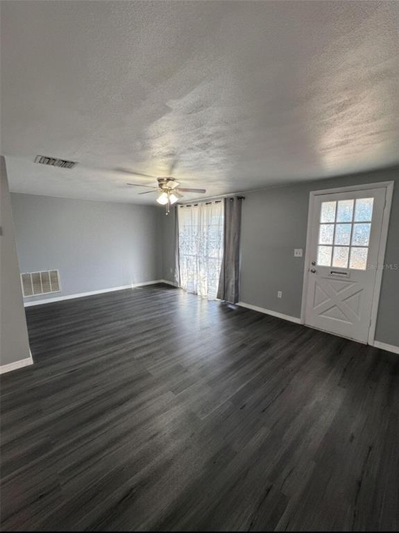 A living room with gray walls, dark wood-look flooring, a ceiling fan, and a front door — 4025 GRAYTON DRIVE, NEW PORT RICHEY, FL