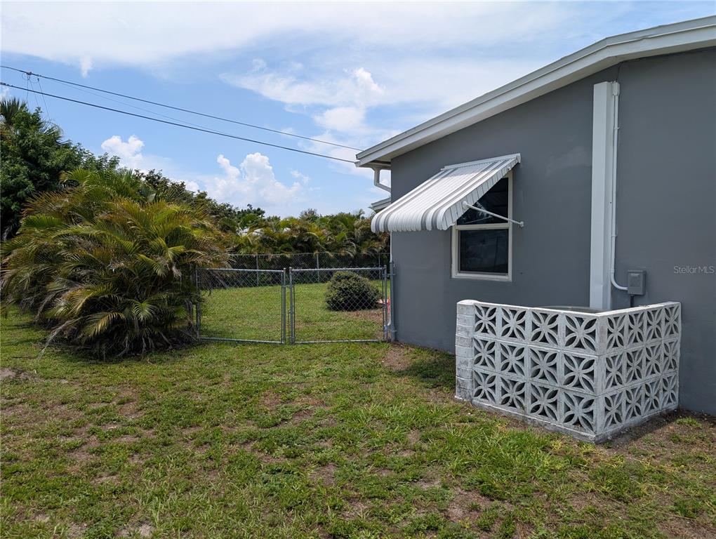 The exterior of a gray house features a metal awning, a decorative block screen, and fencing — 22311 MIDWAY BOULEVARD, PORT CHARLOTTE, FL