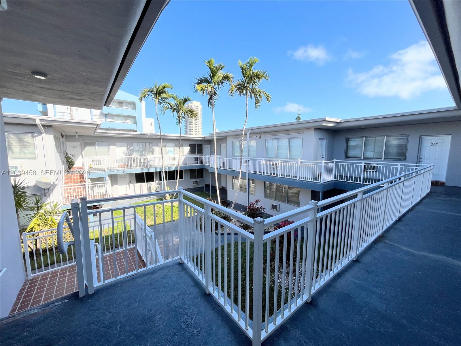 An elevated walkway overlooks a courtyard with palm trees and a small garden area — 350 75th St # 202, Miami Beach FL 33141, MIAMI BEACH, FL