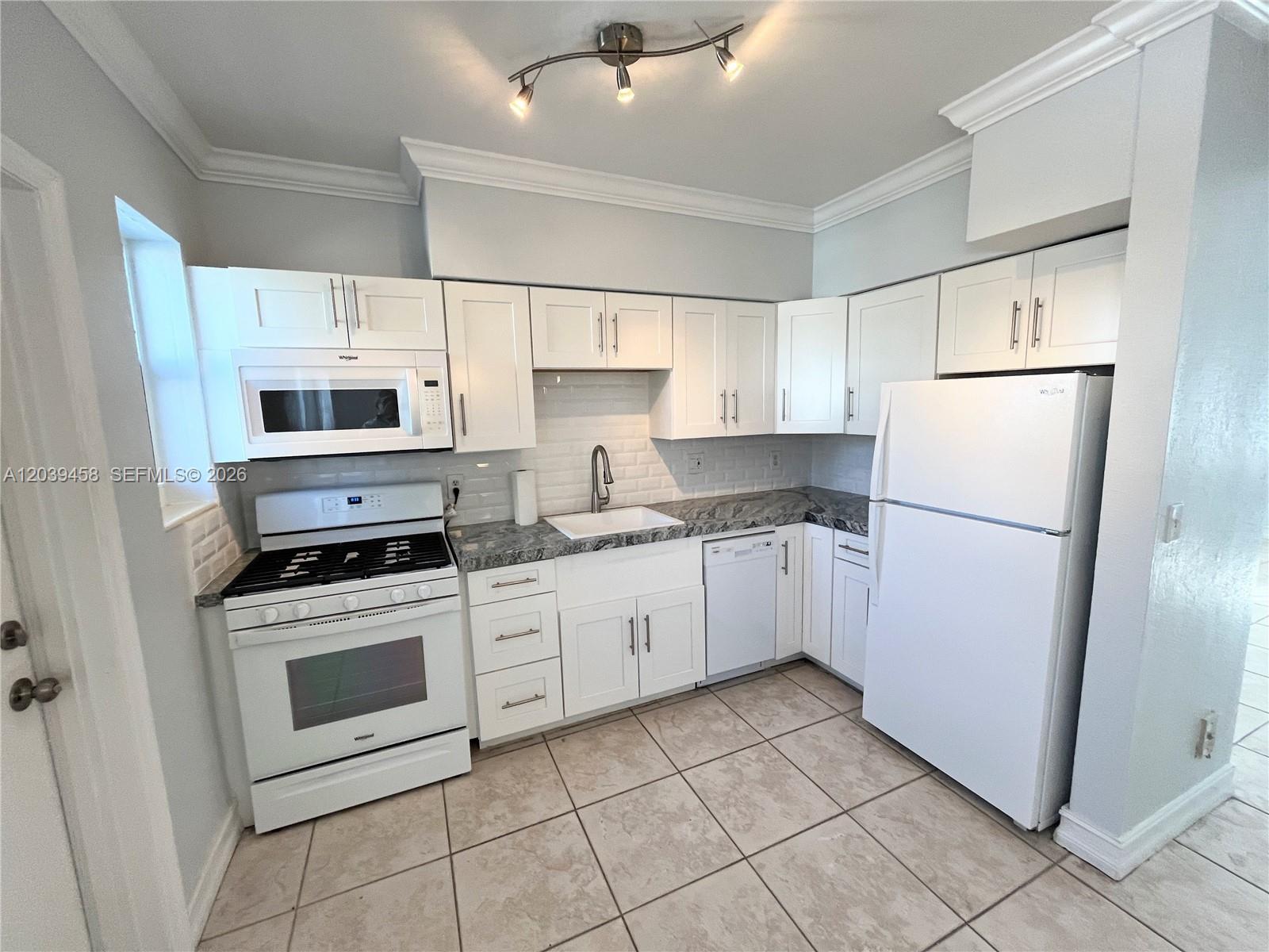 A kitchen features white cabinetry, white appliances, a tiled backsplash, and light-colored floor tiles — 350 75th St # 202, Miami Beach FL 33141, MIAMI BEACH, FL