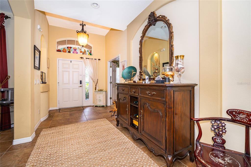 An entryway features tile flooring, a large wooden sideboard, an ornate mirror, and a front door — 124 YELLOW SNAPDRAGON DRIVE, DAVENPORT, FL
