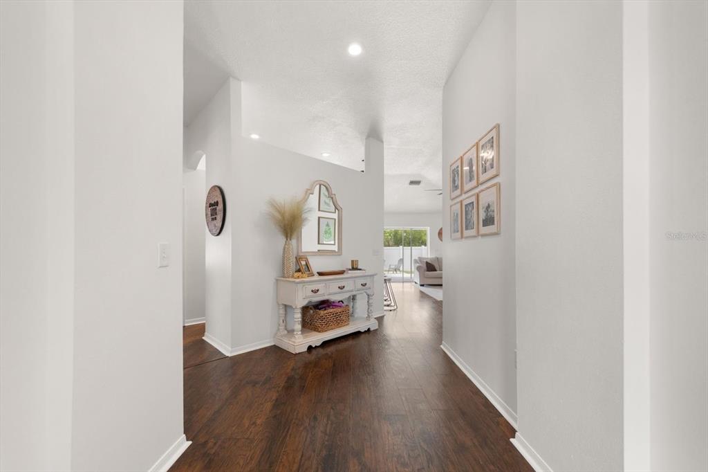 A bright entryway features dark wood flooring, white walls, and a console table with decor — 4529 MARCHMONT BOULEVARD, LAND O LAKES, FL