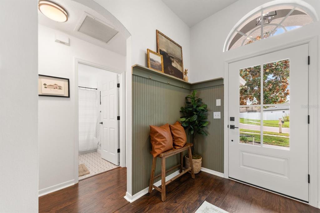 An entryway features dark wood floors, olive green beadboard paneling, a wooden bench, and a door — 4529 MARCHMONT BOULEVARD, LAND O LAKES, FL
