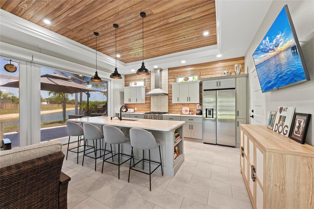 A modern kitchen features a wood-paneled tray ceiling, a large island, and a wall-mounted television — 8115 SW SAND CRANE CIRCLE LOT 2, ARCADIA, FL