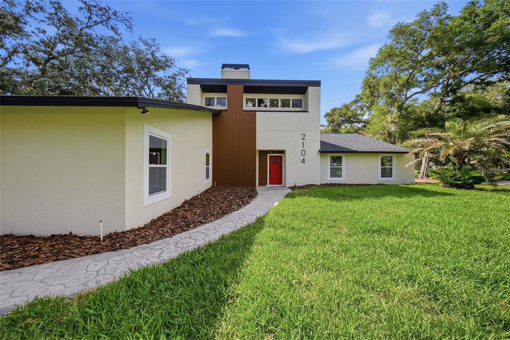 A modern house exterior features a red front door, wood-paneled accent, and stone walkway — 2104 DOEFIELD COURT, VALRICO, FL