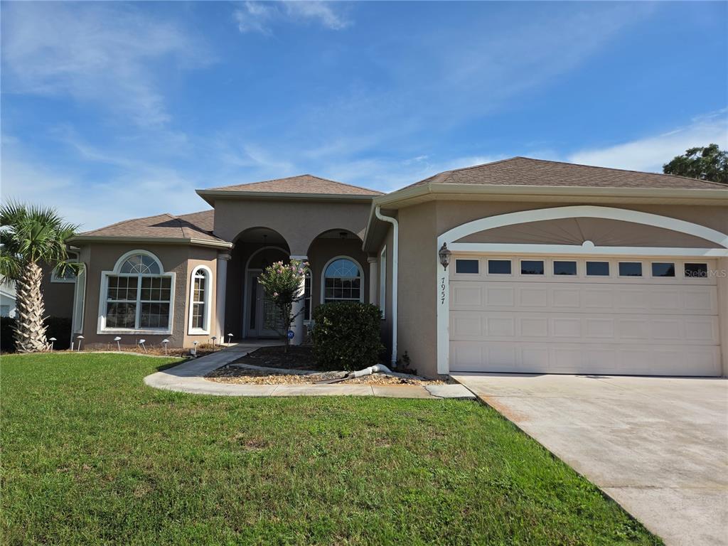A single-story suburban house with a tan stucco exterior, a two-car garage, and a palm tree — 7957 SW 103RD LOOP, OCALA, FL