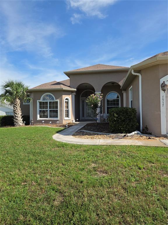 A tan stucco house features arched entryways, a palm tree, and a curved concrete walkway — 7957 SW 103RD LOOP, OCALA, FL