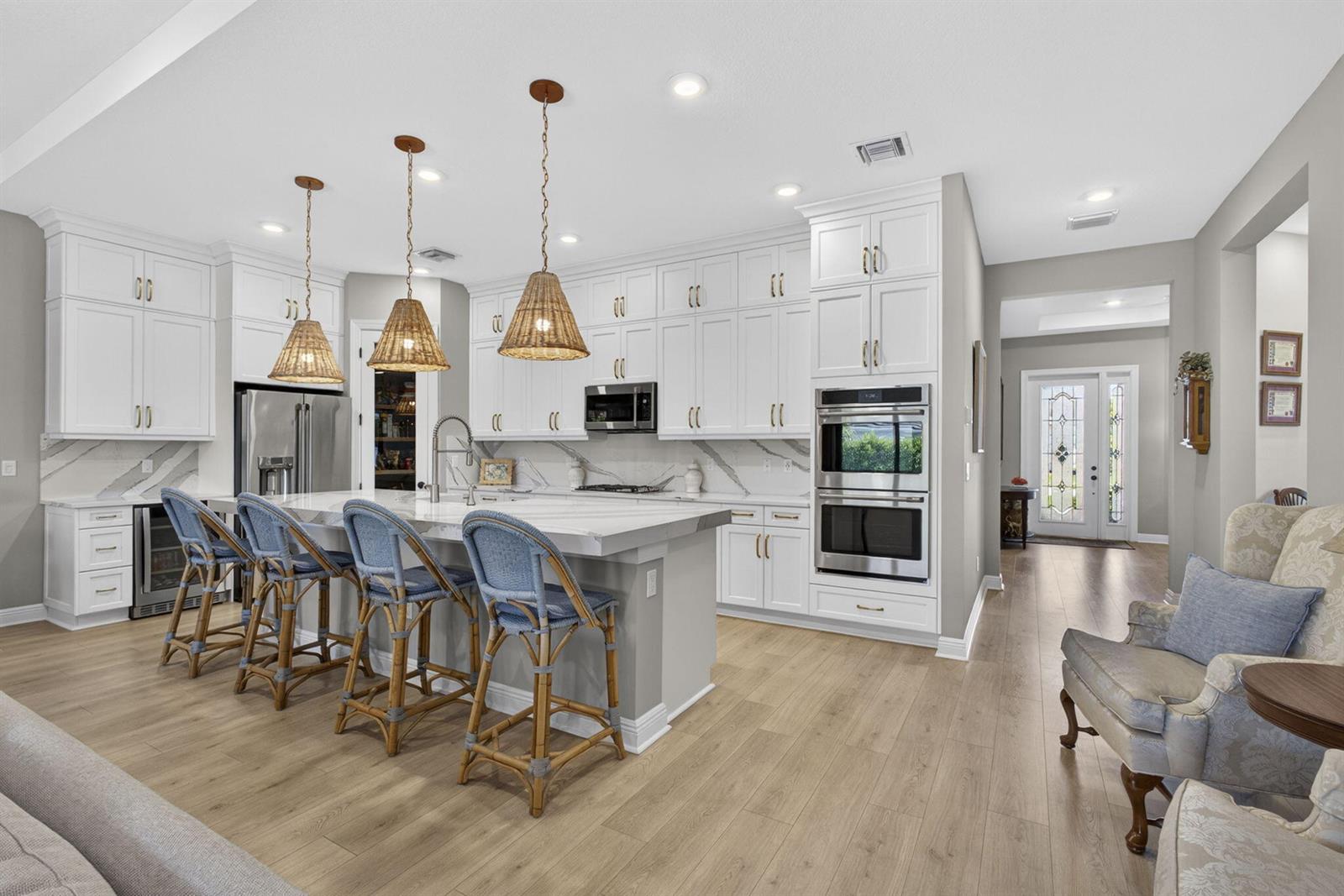 A modern kitchen features white cabinetry, a large marble island, and four blue wicker stools — 15830 Key Biscayne Lane, Westlake FL 33470, WESTLAKE, FL