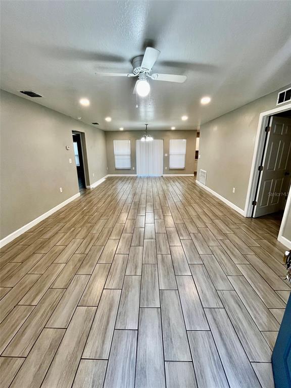A long living room features light wood-look tile flooring, recessed lighting, and a ceiling fan — 1705 3RD STREET NW UNIT A, WINTER HAVEN, FL