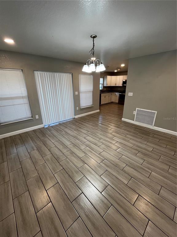 An open-concept dining area features wood-look tile flooring, a chandelier, and a view of the kitchen — 1705 3RD STREET NW UNIT A, WINTER HAVEN, FL