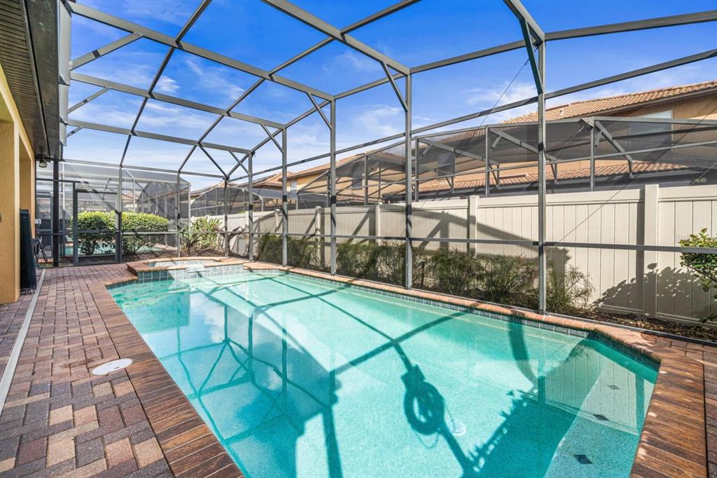 A rectangular swimming pool with a spa is enclosed by a screened lanai and pavers — 8879 MENTON LOOP, KISSIMMEE, FL