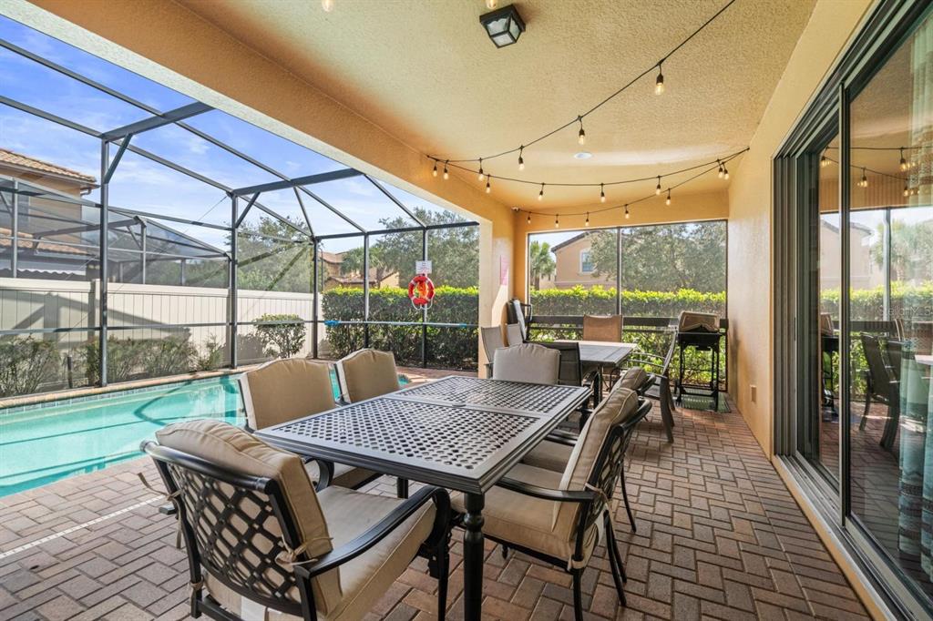 A covered patio with a dining set, string lights, and a screened-in swimming pool — 8879 MENTON LOOP, KISSIMMEE, FL