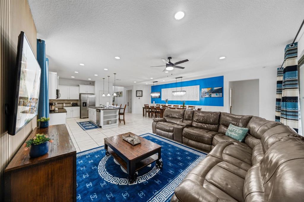 An open-concept living room and kitchen featuring a large brown sectional, blue rug, and dining area — 8879 MENTON LOOP, KISSIMMEE, FL