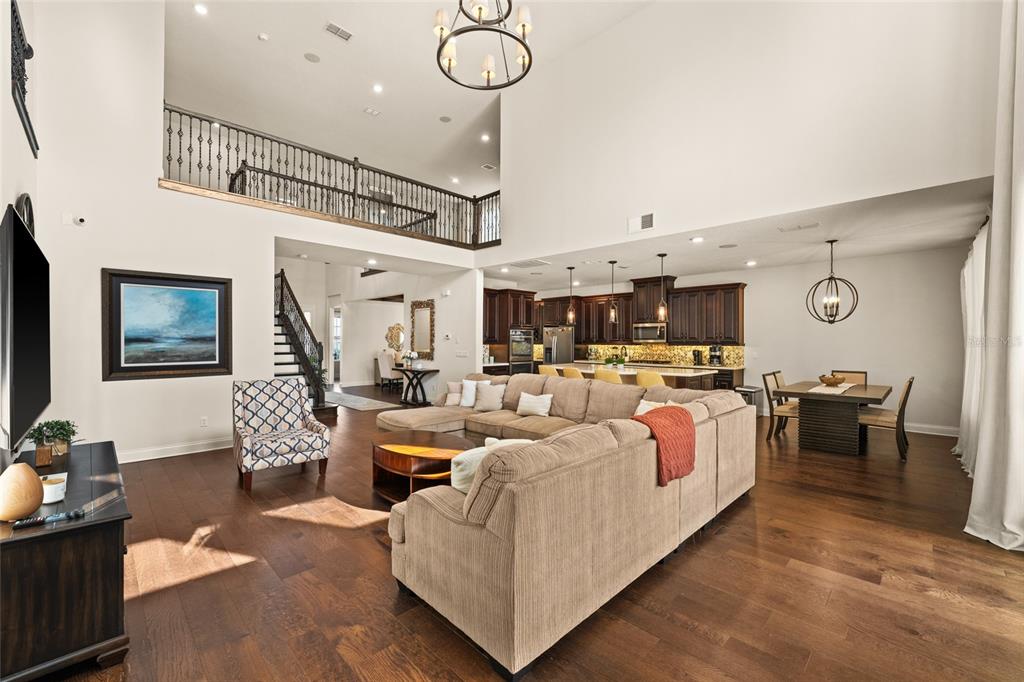 A spacious open-concept living room features a large sectional, hardwood floors, and a lofted balcony — 13596 GORGONA ISLE DRIVE, WINDERMERE, FL