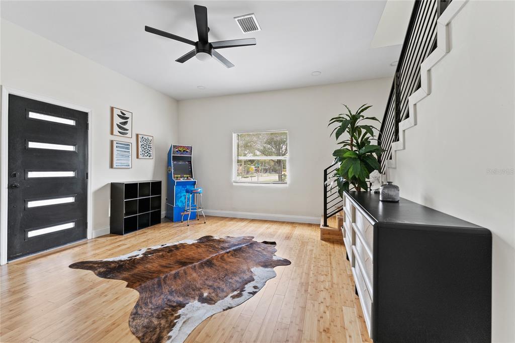 A room with light wood floors, a cowhide rug, an arcade cabinet, and a staircase — 680 25TH AVENUE S, ST PETERSBURG, FL