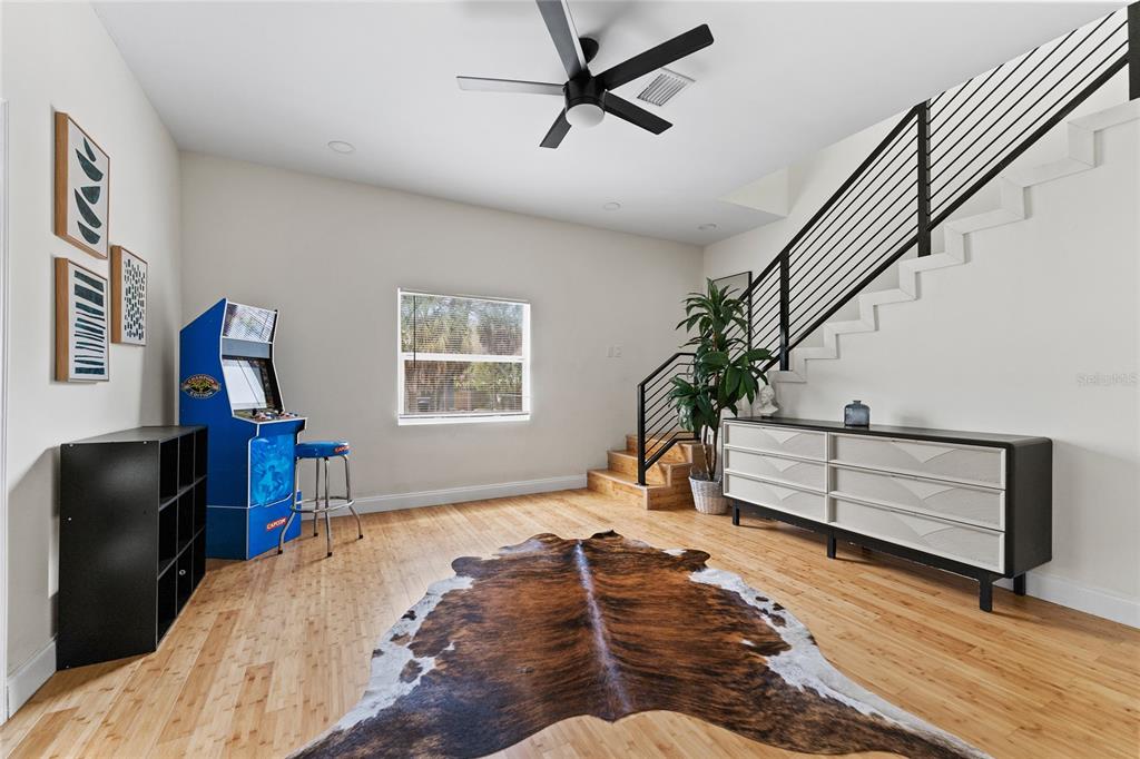 A room with light wood flooring, a staircase, an arcade cabinet, and a cowhide rug — 680 25TH AVENUE S, ST PETERSBURG, FL