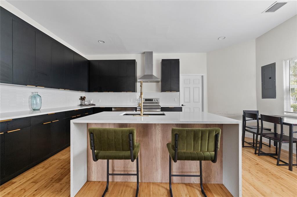 A modern kitchen features black cabinets, a white quartz island with green stools, and wood flooring — 680 25TH AVENUE S, ST PETERSBURG, FL