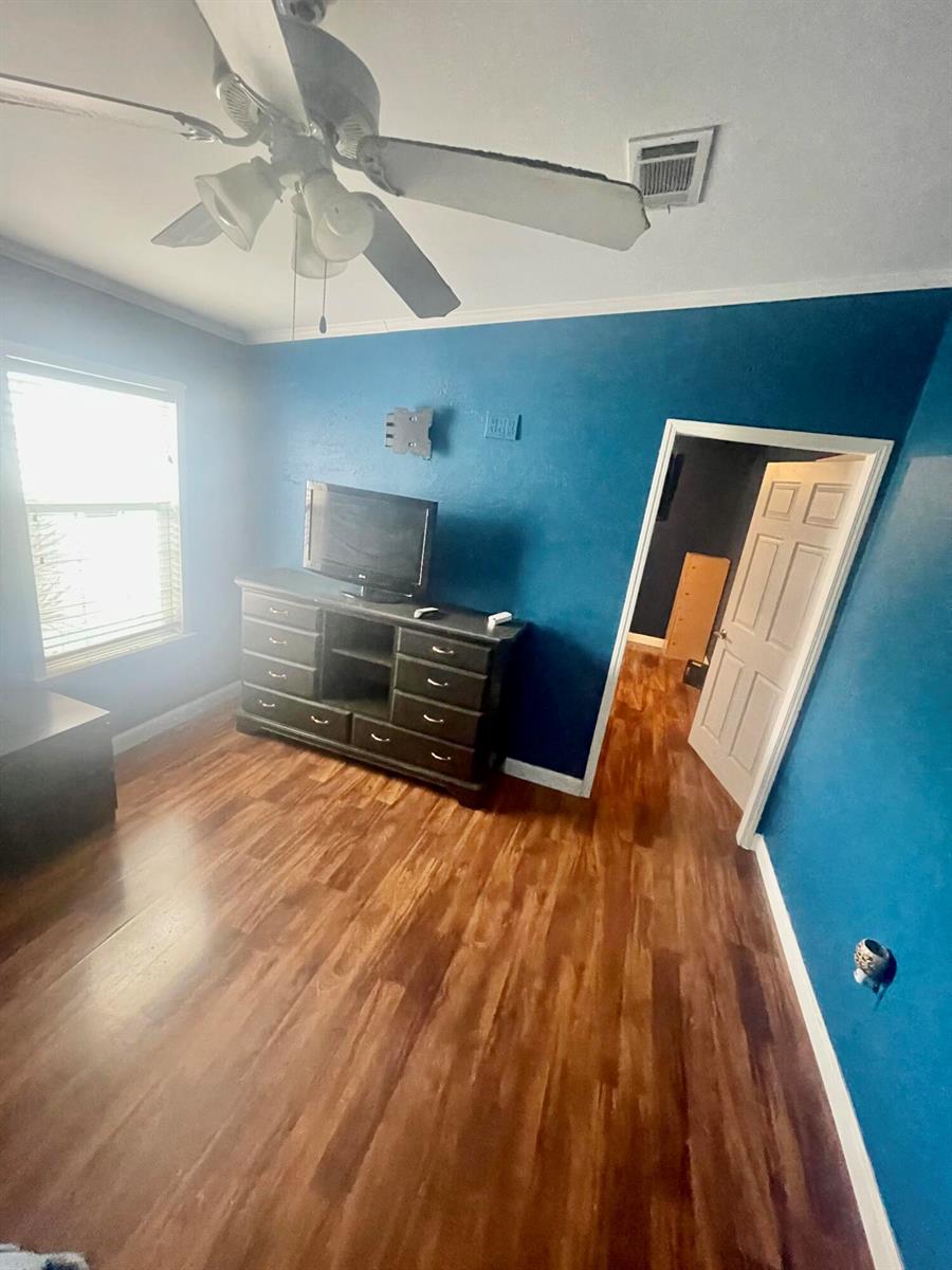 A bedroom with blue walls, wood-look flooring, a ceiling fan, and a television on a dresser — 195 Plantation Boulevard, Lake Worth FL 33467, LAKE WORTH, FL