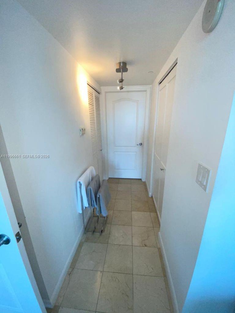 A narrow hallway features light-colored tile flooring, white walls, and a closed white door — 2101 Brickell Ave # 2604, Miami FL 33129, MIAMI, FL
