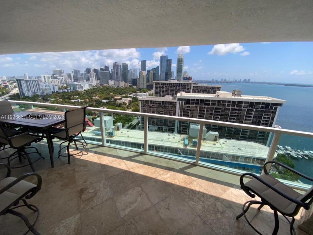 A balcony with stone flooring and patio furniture overlooks a city skyline and bay — 2101 Brickell Ave # 2604, Miami FL 33129, MIAMI, FL