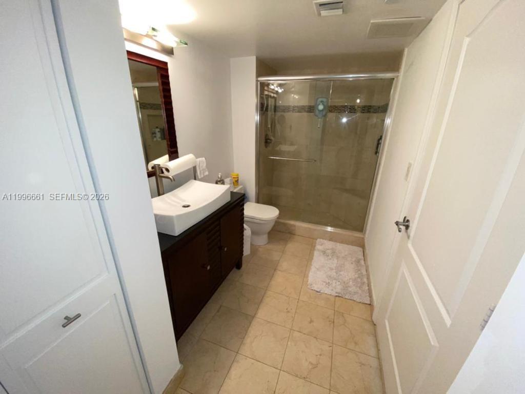 A bathroom features a vessel sink vanity, a glass-enclosed shower, and beige tile flooring — 2101 Brickell Ave # 2604, Miami FL 33129, MIAMI, FL