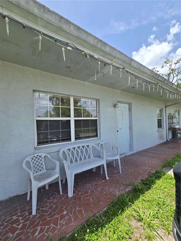 A white stucco exterior features a tiled porch with plastic seating and hanging holiday lights — 2150 BARBARA DRIVE UNIT 2, ST CLOUD, FL