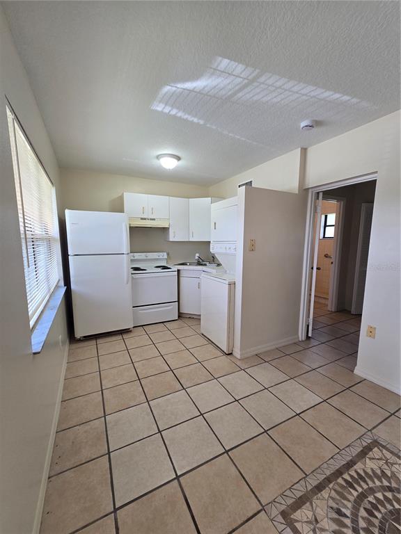 A small kitchen features white appliances, tile flooring, and a stacked washer and dryer unit — 2150 BARBARA DRIVE UNIT 2, ST CLOUD, FL