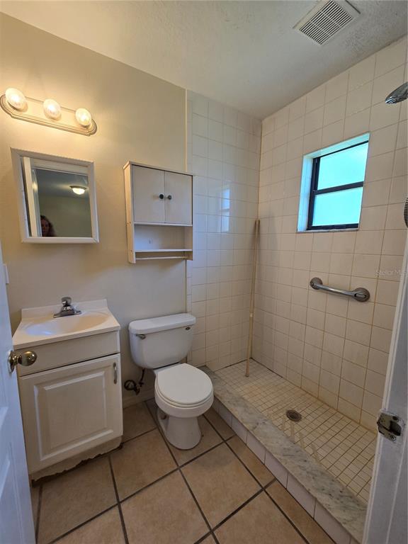 A bathroom features a white vanity, a toilet, and a tiled walk-in shower with grab bars — 2150 BARBARA DRIVE UNIT 2, ST CLOUD, FL