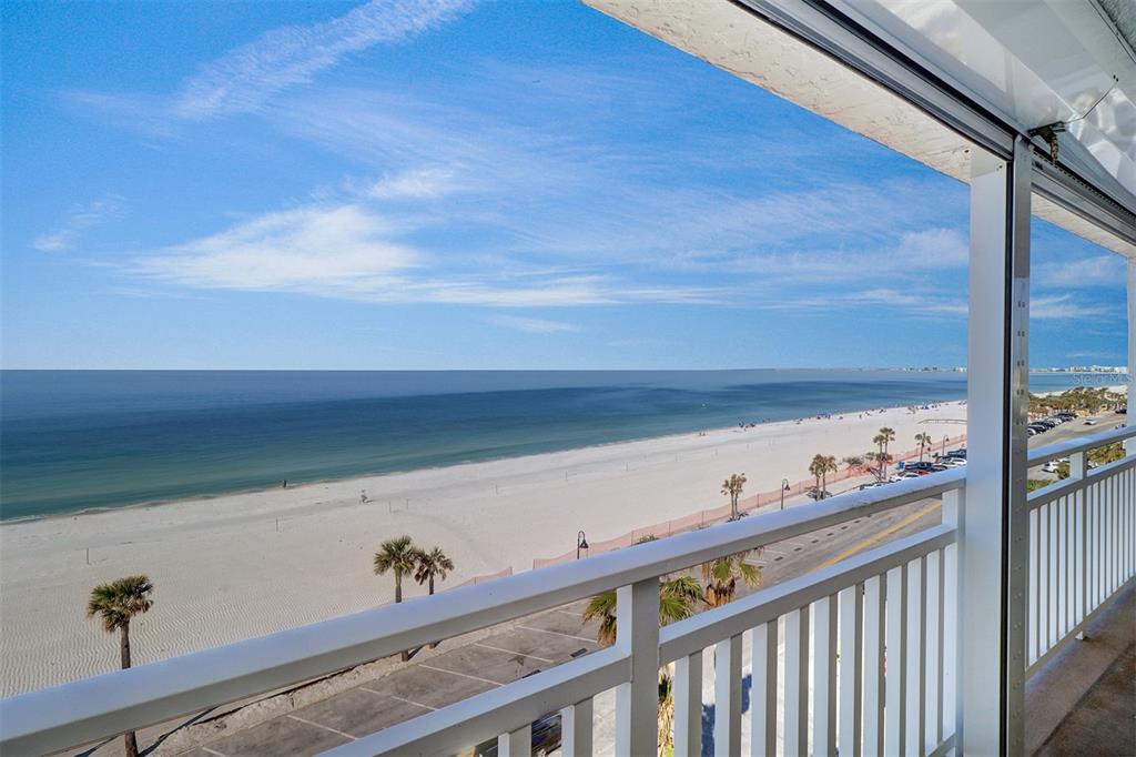 A balcony view overlooking a sandy beach, the ocean, and a coastal road with palm trees — 555 GULF WAY UNIT 7N, ST PETE BEACH, FL