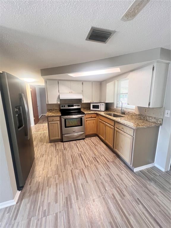 A kitchen features wood-tone lower cabinets, white upper cabinets, granite countertops, and stainless steel appliances — 9910 LAKE CHRISE LANE, PORT RICHEY, FL