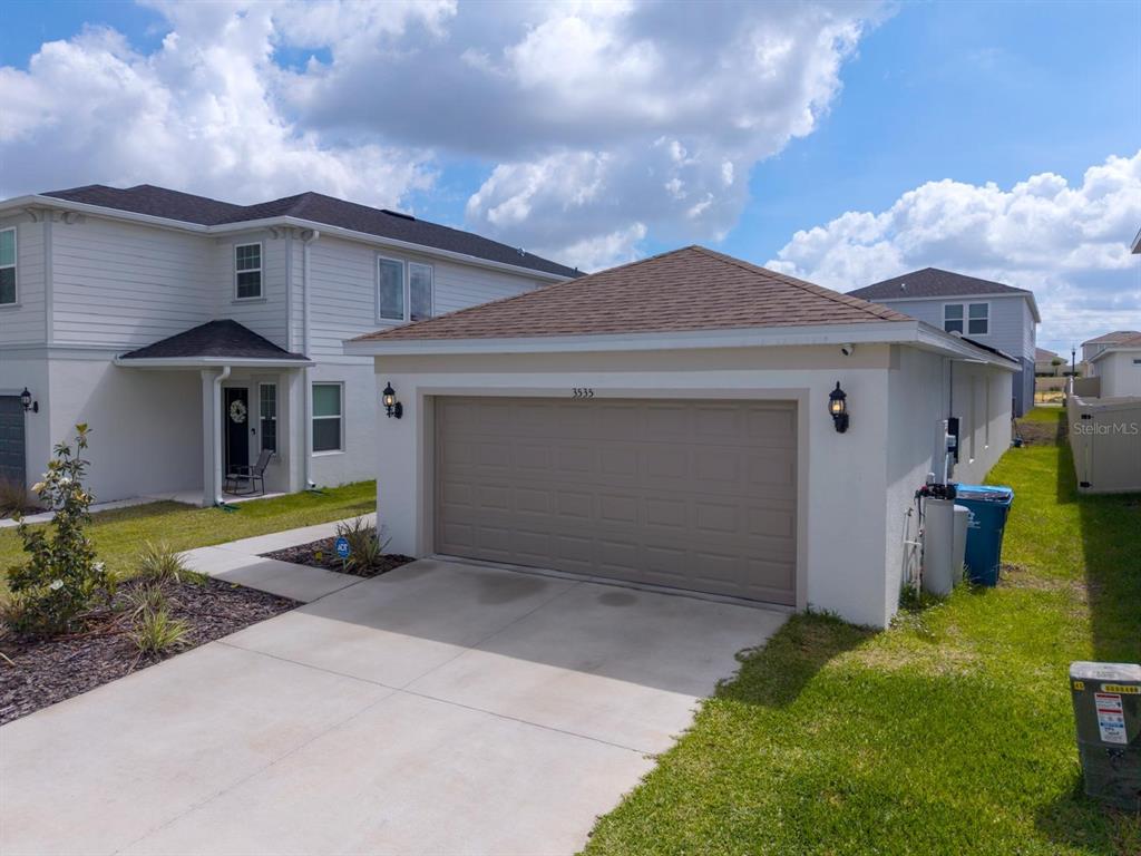 A detached garage with a tan door sits next to a two-story white house — 3535 WEAVER WAY, DAVENPORT, FL