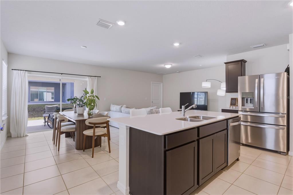 An open-concept kitchen and dining area features dark cabinetry, a quartz island, and tile flooring — 3535 WEAVER WAY, DAVENPORT, FL