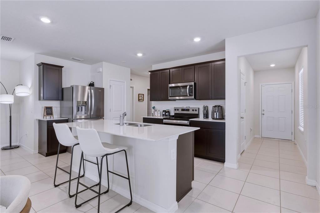A kitchen features dark wood cabinets, white countertops, a central island, and stainless steel appliances — 3535 WEAVER WAY, DAVENPORT, FL