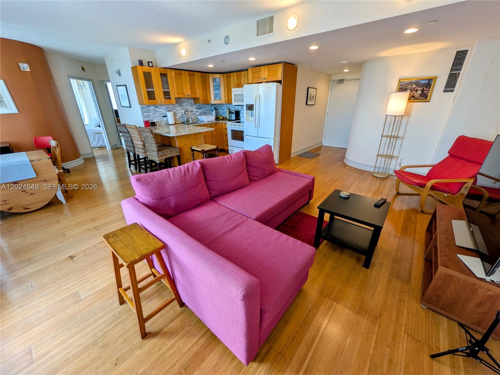 An open-concept living area features a pink sectional sofa, kitchen with wood cabinets, and hardwood floors — 1720 Harrison St # 14D, Hollywood FL 33020, HOLLYWOOD, FL