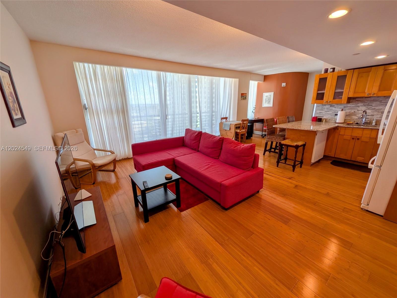 An open-concept living area features a red sectional sofa, hardwood floors, and an adjacent kitchen — 1720 Harrison St # 14D, Hollywood FL 33020, HOLLYWOOD, FL