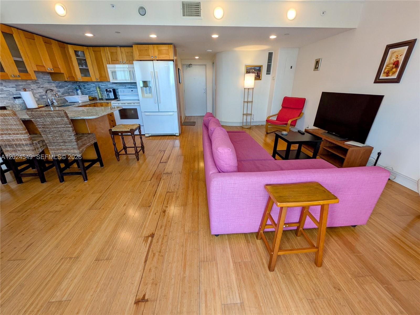 An open-concept living room and kitchen feature hardwood floors, a pink sofa, and wooden cabinetry — 1720 Harrison St # 14D, Hollywood FL 33020, HOLLYWOOD, FL