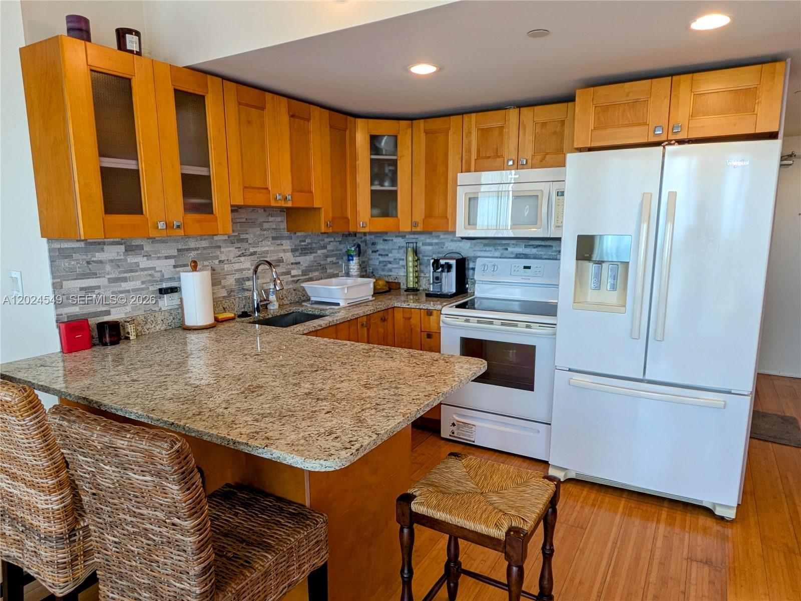 A kitchen features light wood cabinets, granite countertops, a white refrigerator, and a breakfast bar — 1720 Harrison St # 14D, Hollywood FL 33020, HOLLYWOOD, FL