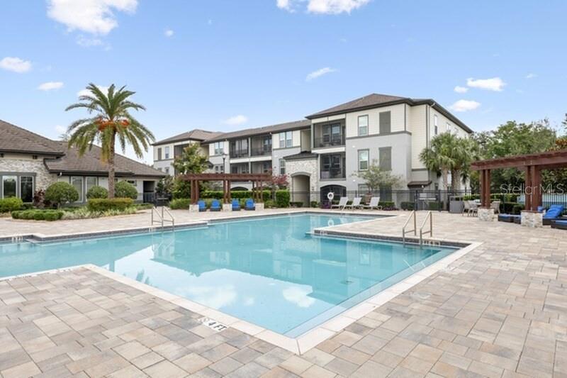 A swimming pool sits in front of a multi-story apartment building with a patio area — 11128 GRANDE PINES CIRCLE UNIT Palm, ORLANDO, FL