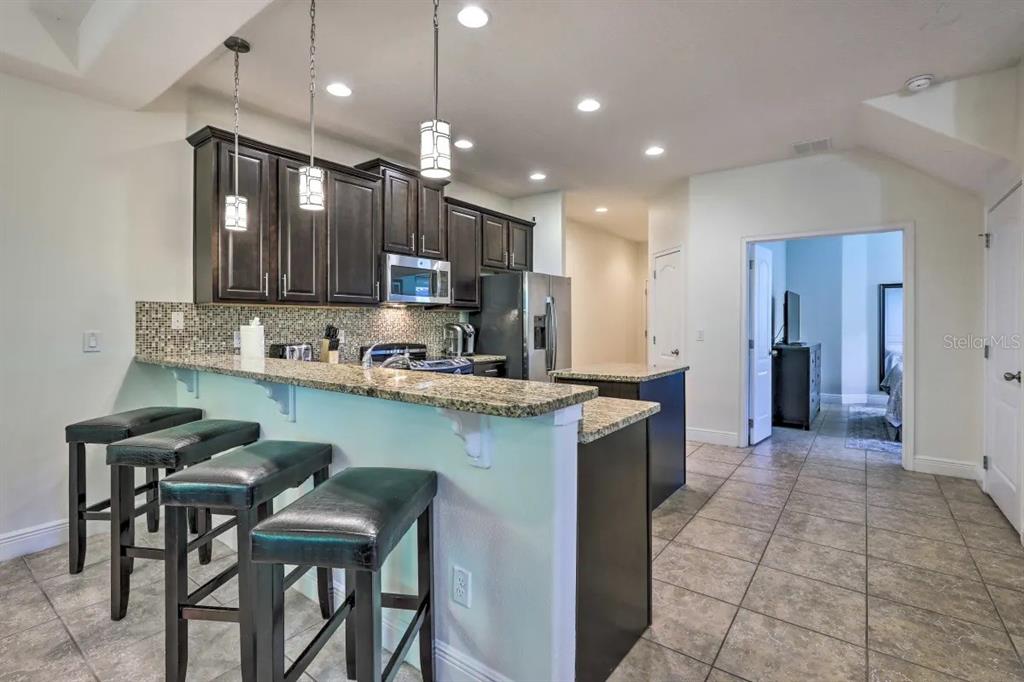 A kitchen features dark wood cabinets, granite countertops, a breakfast bar, and tile flooring — 8147 ROSEVILLE BOULEVARD, DAVENPORT, FL