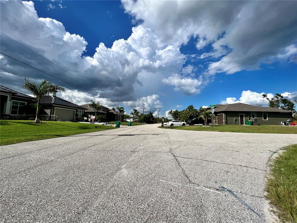 A residential street view featuring houses, green lawns, and a cloudy blue sky — 13463 FROST LANE, PORT CHARLOTTE, FL