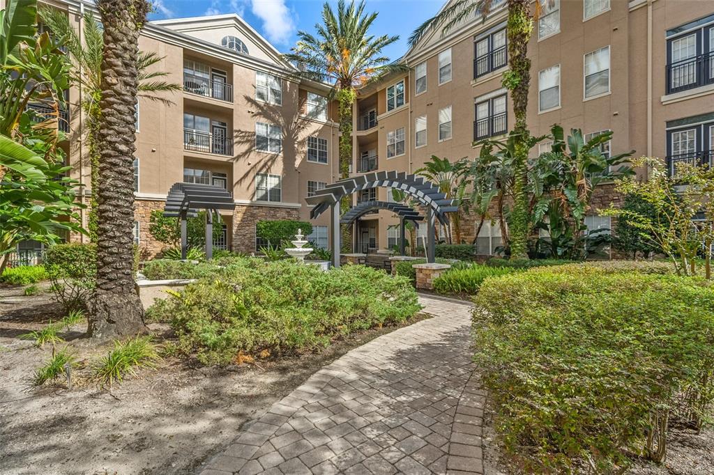 A paved walkway leads through a landscaped courtyard toward a multi-story apartment building with pergolas — 4221 W SPRUCE STREET UNIT 2423, TAMPA, FL