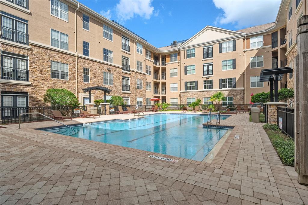 An outdoor swimming pool is surrounded by a paved deck and a multi-story apartment building — 4221 W SPRUCE STREET UNIT 2423, TAMPA, FL