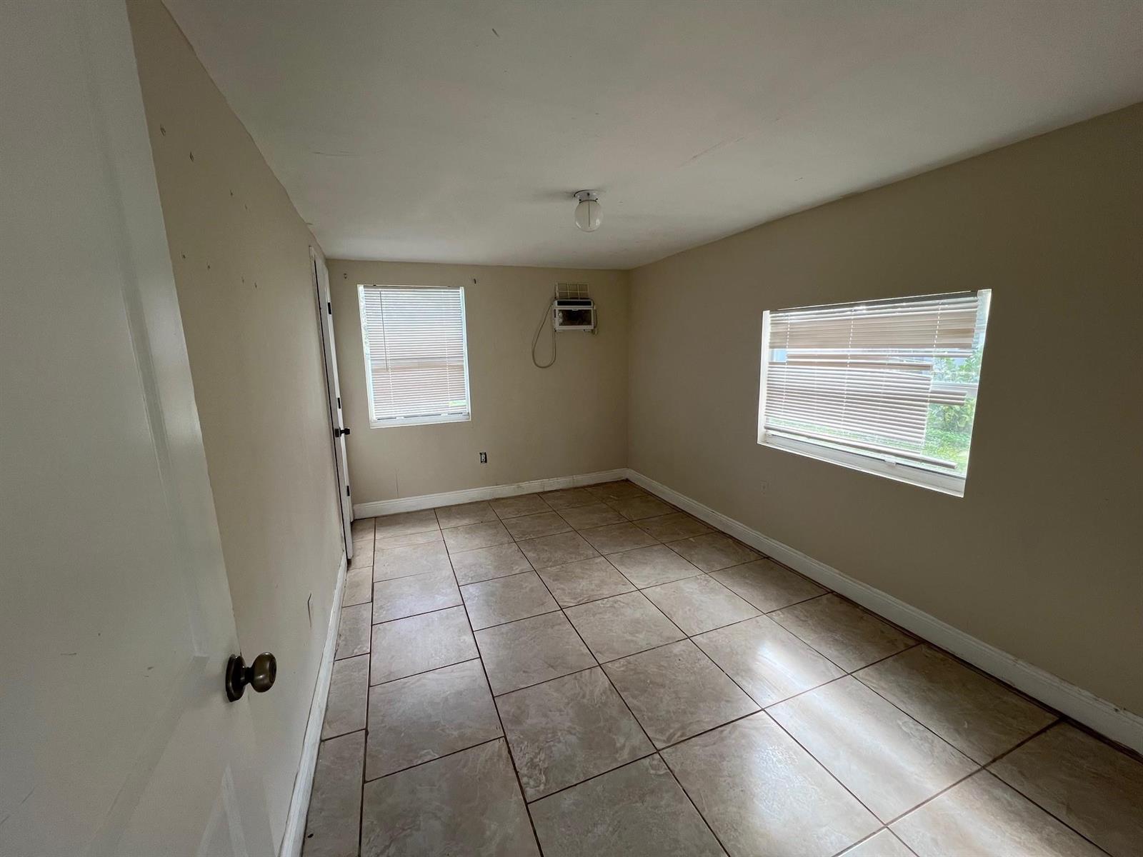 An empty room with beige walls, tile flooring, two windows, and a wall-mounted air conditioner — 8269 NW 1st Place # 2, Miami FL 33150, MIAMI, FL