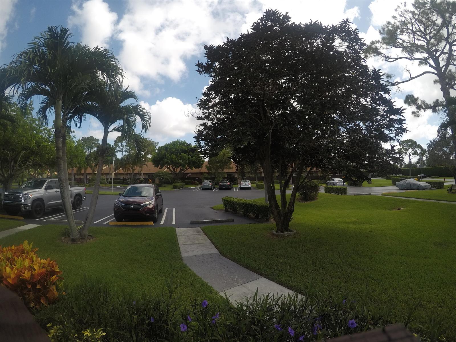 A parking lot with several cars sits in front of a building with palm trees — 633 Sea Pine Way # C, FL 33415, FL