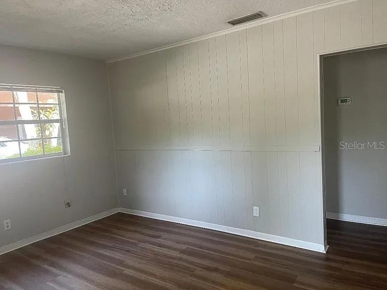 An empty room features light-colored wood-paneled walls, a window, and dark wood-look flooring — 1701 NE 28TH AVENUE, GAINESVILLE, FL