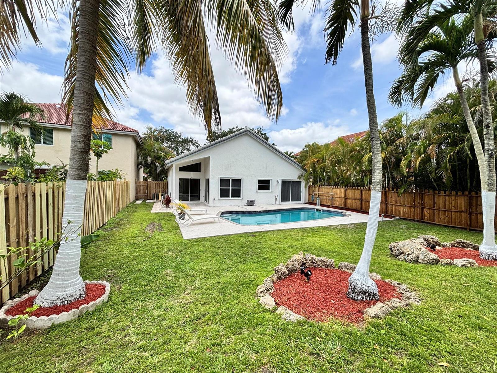 A backyard features a swimming pool, a white house, palm trees, and a wooden fence — 2990 NW 68th Avenue, Margate FL 33063, MARGATE, FL